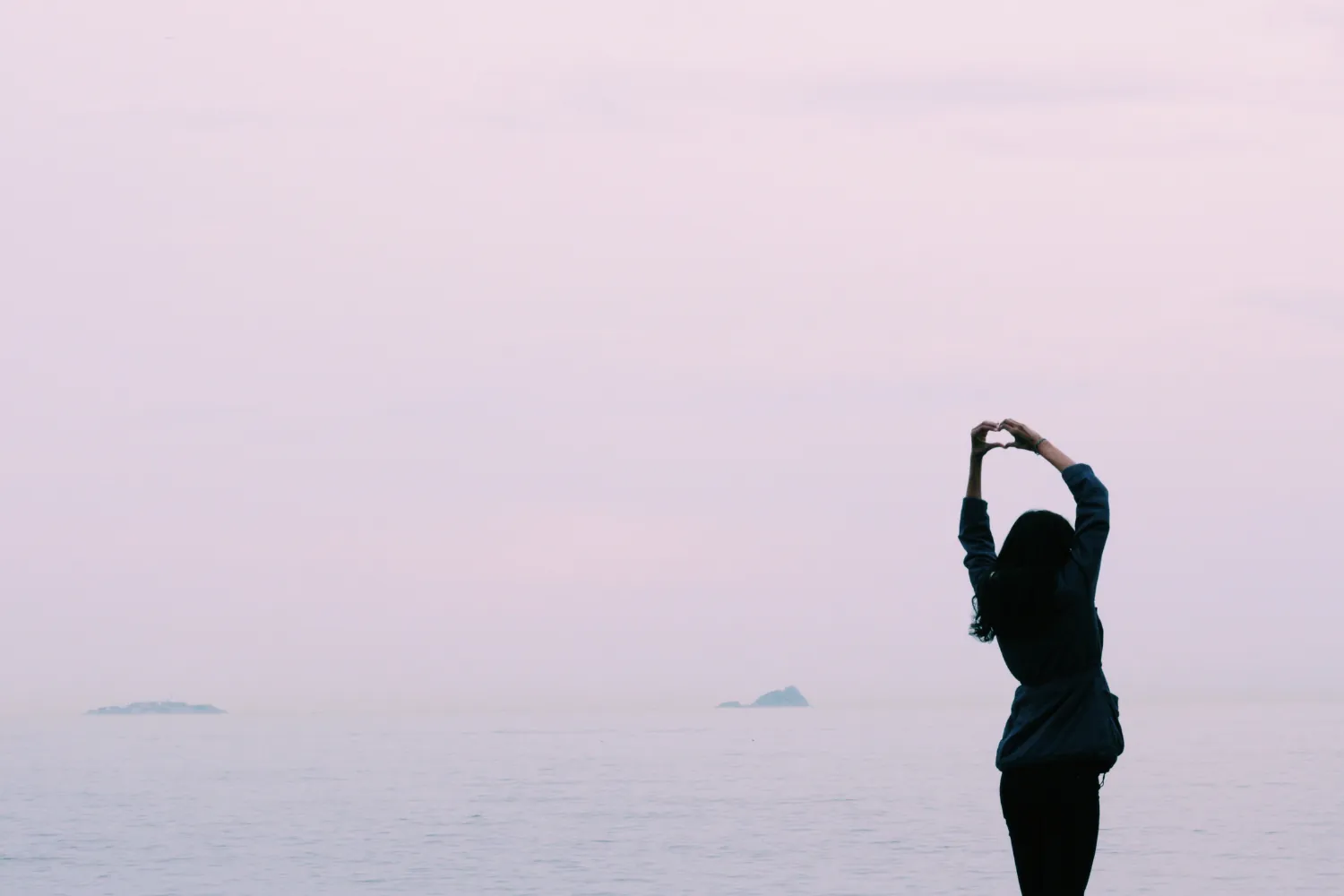 Silhouette d'une femme qui s'étire face à la mer, dans une lumière pâle