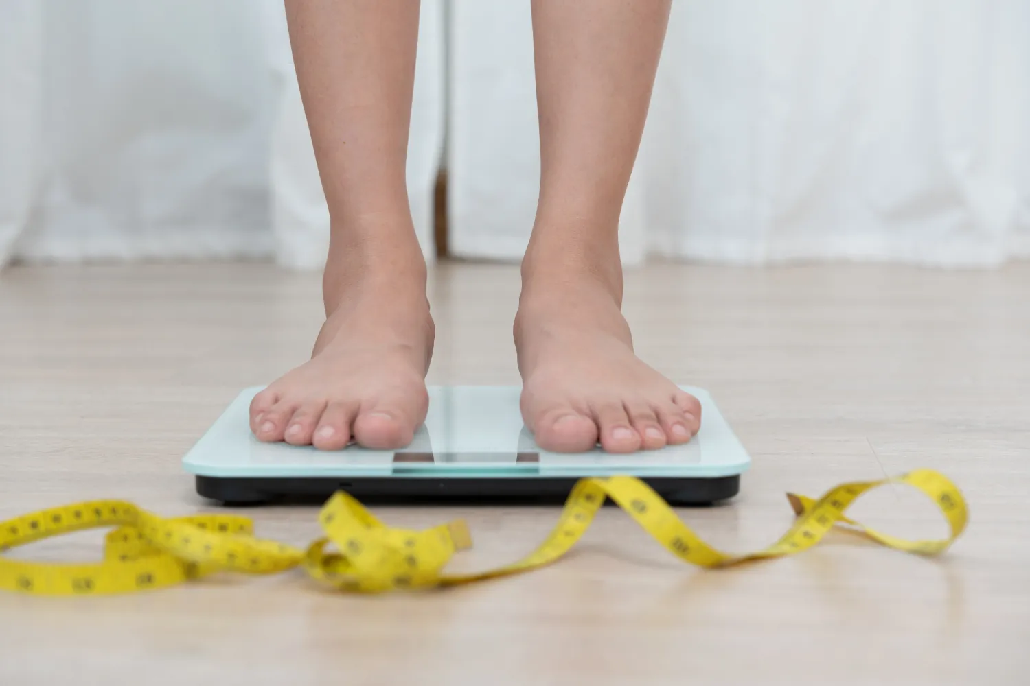 Pieds nus sur une balance, un mètre ruban jaune posé au sol