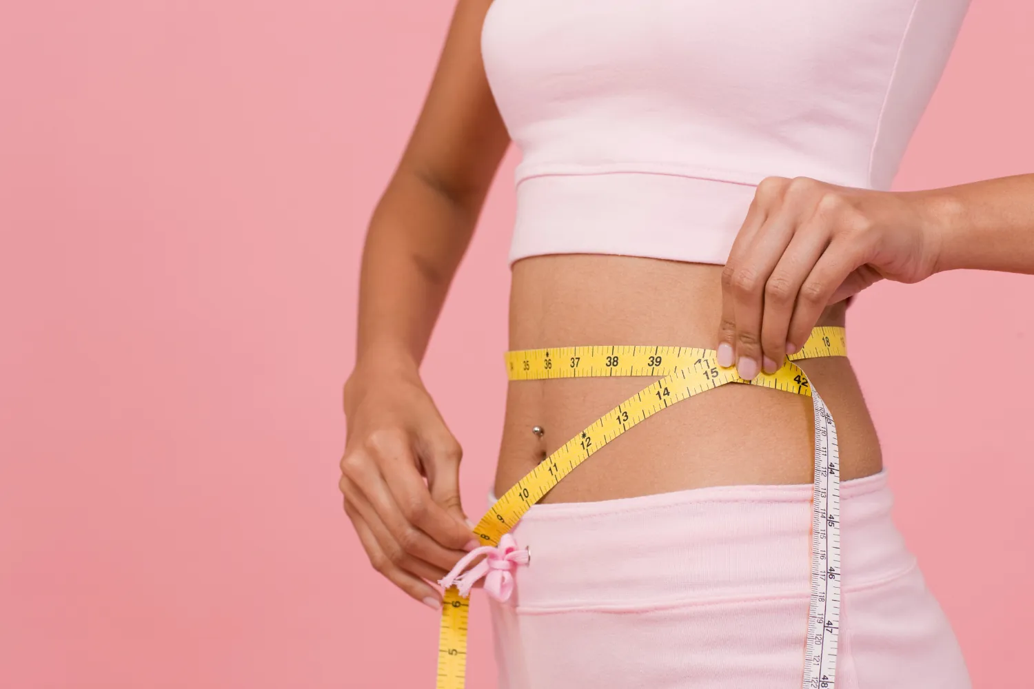Femme en tenue rose qui mesure son tour de taille avec un mètre ruban jaune